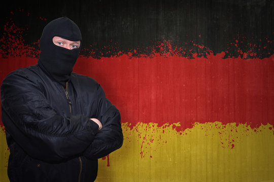 dangerous man in a mask standing near a wall with painted national flag of germany