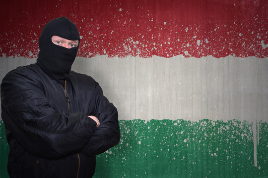 dangerous man in a mask standing near a wall with painted national flag of hungary