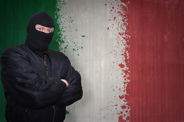 dangerous man in a mask standing near a wall with painted national flag of italy