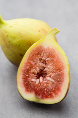 Whole figs and one fig sliced in half on top of a gray table.