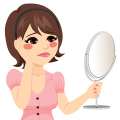 Young woman with sad expression looking herself in a mirror unhappy