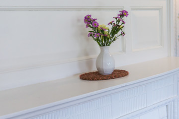 small pink and yellow flower arrangement in white vase on mantel 
