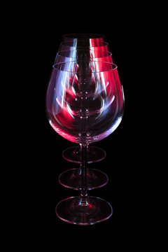 Party wine glasses in nightclub lit by red, blue, lilac lights, nightlife and entertainment industry, objects in row isolated on black background 