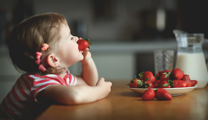 happy child girl eats strawberries in summer home kitchen