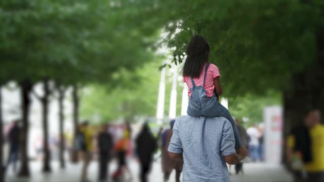 African American father and daughter walking away from camera in urban park