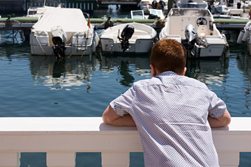 Niño mirando los barcos en puerto deportivo.