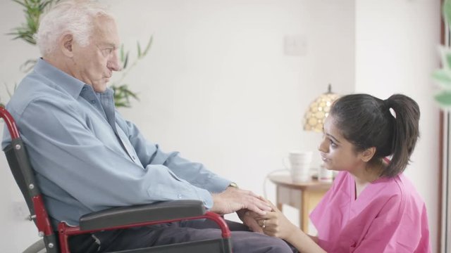  Caring home support nurse comforting sad elderly man in a wheelchair