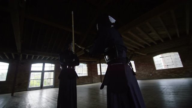 Japanese kendo fighters with bamboo swords competing in dark industrial building