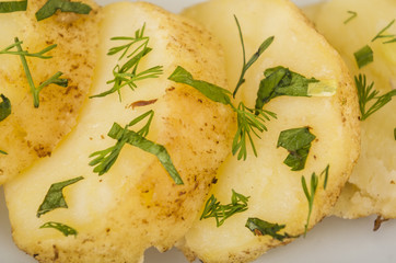 Delicious sliced potato pieces cooked to perfection, piled up on white plate with green herbal topping