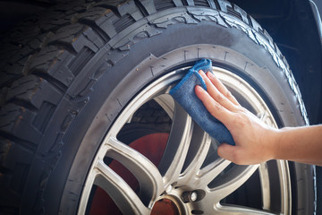 Man's hand holding a blue fabric cleaning car tires and wheels
