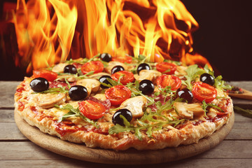 Delicious hot pizza on wooden table against fire flame background