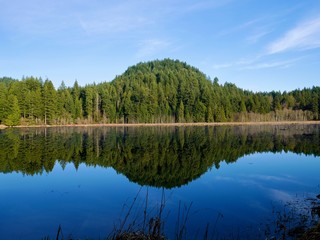 Fototapeta na wymiar Green Hills Reflection in Calm Water. Northeast Coquitlam, British Columbia, alongside Pitt-Addington Marsh and the Pitt River. Canada. 