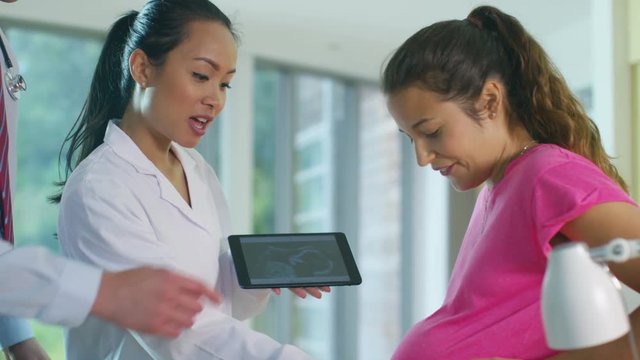  Medical staff examining pregnant woman and showing her a scan of the baby