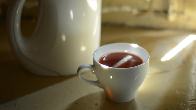 Cup of hot tea on a background of the teapot. Out of the darkness comes a cup of tea