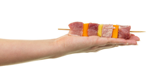 Female hand holding  skewer with slices  raw meat and vegetables.