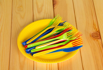 Yellow disposable plates with colored plastic knives, forks.