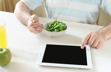 Man eating salad and working using tablet computer