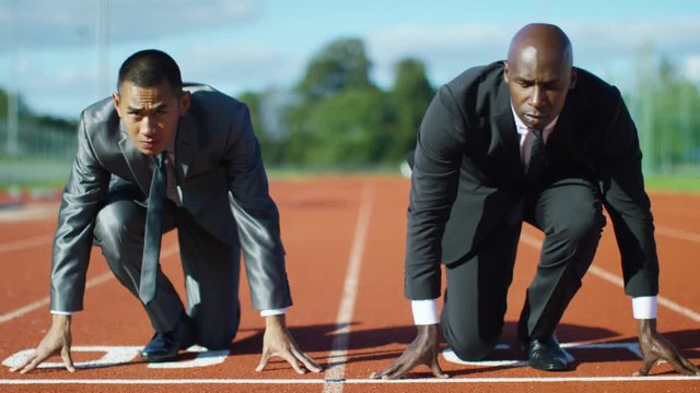  Competitive businessmen at running track line up at starting line before race