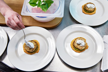 Cook puts the sour cream in dish with fish cutlet