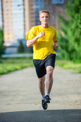 Running man jogging in city street park at beautiful summer day. Sport fitness model caucasian ethnicity training outdoor.