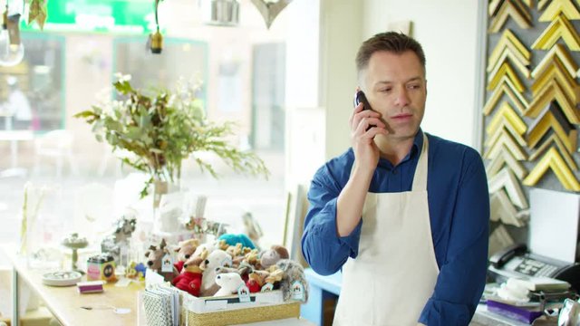  Cheerful business owner makes a phone call behind the counter of his shop