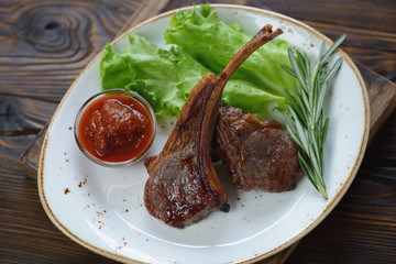 Plate with grilled lamb chops, fresh green salad and a dip sauce