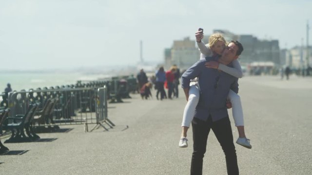 Happy fun couple playing piggyback pause to take a selfie on mobile phone