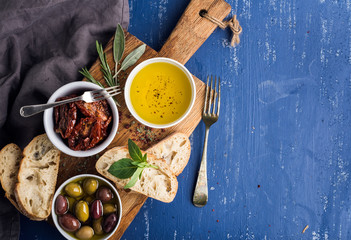 Mediterranean snacks set. Olives, oil, herbs and sliced ciabatta bread on yellow rustic oak board...