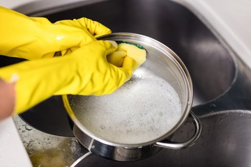 Woman wearing gloves washing utensils at home