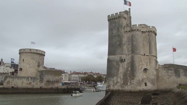 Tilt shot up the harbour towers of La Rochelle in France as a small boat returns to port