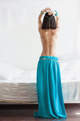 Attractive an slim woman in oriental garment and golden jewelry with henna drawnings on her back. She wears turquoise skirt and golden belt. She has a beautiful belly and perfect tanned skin.