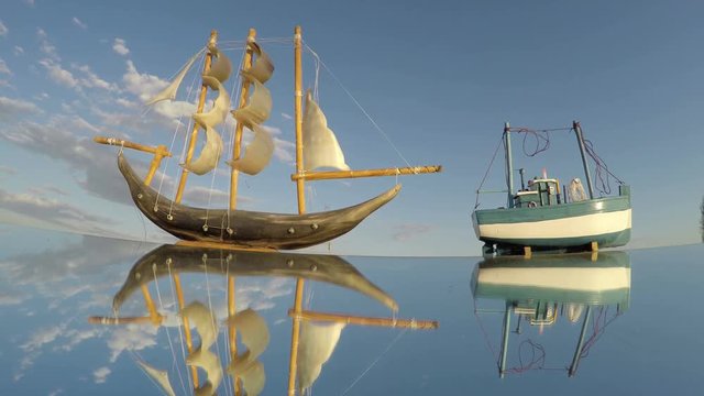Two toy ships on a mirror reflecting sky on sunny cloudy day, time lapse 4K