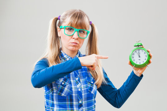 Studio shot portrait of nerdy woman who is pointing at clock that shows five to twelve time