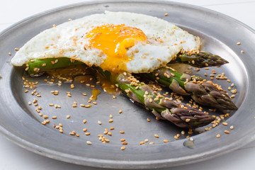 Asparagus with roasted sesame and fried egg on rustic iron plate.