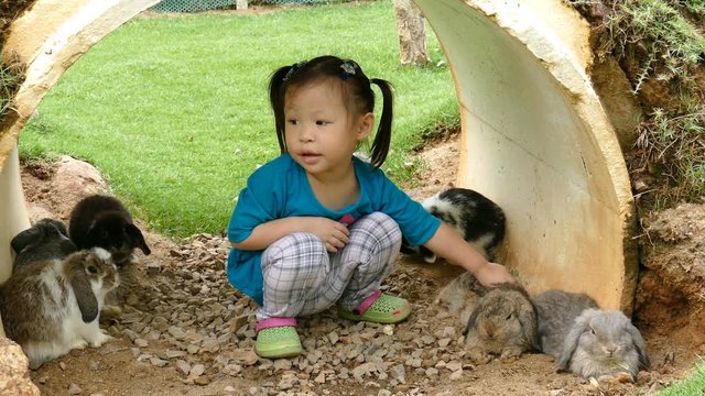Little girl with real rabbit. Child playing with pet bunny. Kids play with animals. 

