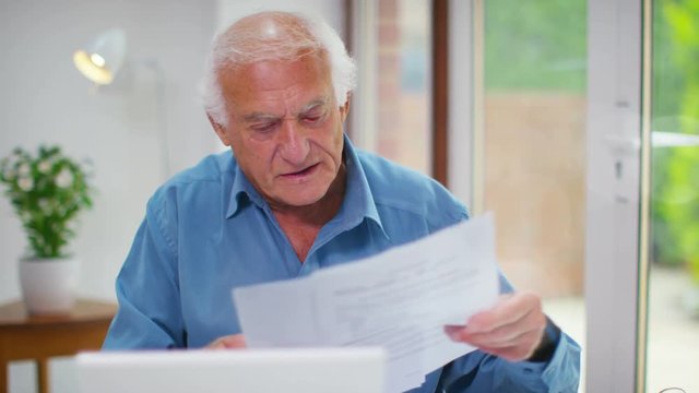  Happy senior man working on a laptop computer & looking at paperwork