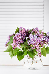 Beautiful lilac flowers in glass vase on white shutters