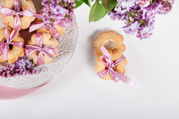 Obraz na płótnie Canvas Biscuits with pink ribbon on white plate with lilac flowers, top