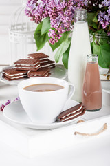 Cup of coffee and few bottles of milk on  a white tray with lila