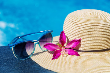 Blue sunglasses and straw hat with orchid flower near swimming pool - holiday concept