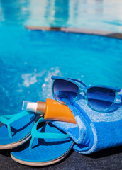 Blue slippers, sunsscreen cream and sun glasses near swimming pool - holiday concept