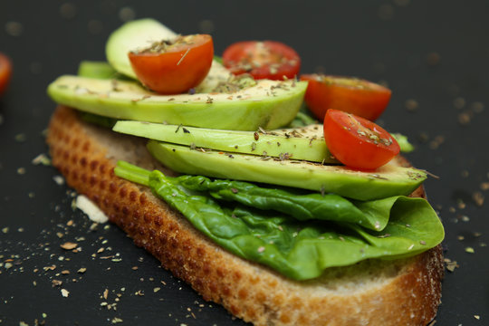 Close up of toast with spinach leaves, avocado and tomatoes.
