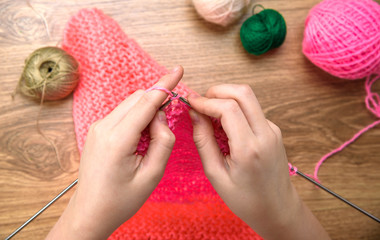 baby girl knitting pink scarf close up on wooden table.