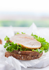 Homemade tasty sandwich with salad leaves and ham on a cutting board on a kitchen background, with place for text, selective focus