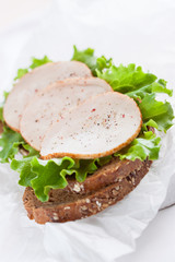 Homemade tasty sandwich with salad leaves and ham on a cutting board on a kitchen background, closeup, selective focus.