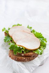Homemade tasty sandwich with salad leaves and ham on a cutting board on a kitchen background with free space for text, closeup, selective focus