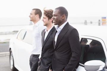 Well dressed men posing leaning on a limousine