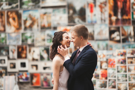 Gorgeous wedding couple, bride, groom kissing and hugging against the background of paintings