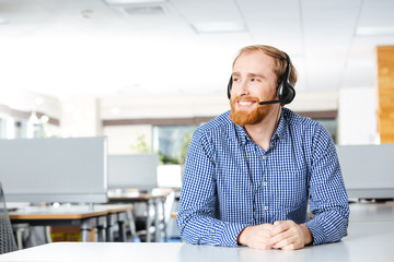 Cheerful man sitting and using headset in office