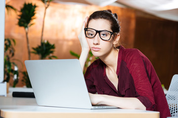 Exhausted businesswoman in glasses using laptop on workplace